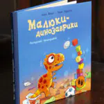 Малюки-динозаврики. Расмусове прибирання — книга Ларса Мелє на дерев'яному столі
