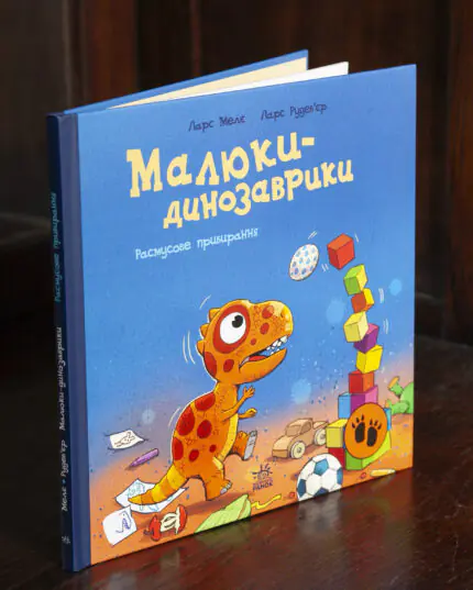 Малюки-динозаврики. Расмусове прибирання — книга Ларса Мелє на дерев'яному столі
