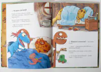 Two-page illustration: dinosaurs waking up in a cozy bedroom; a blue dinosaur sits up under a blue blanket while an orange spotted dinosaur sleeps in bed, with a dresser, mug, and glasses nearby.
