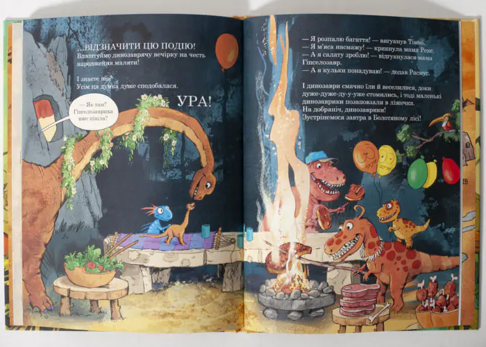 Colorful dinosaur party scene in a cave, with friends gathered around a campfire and a cake with balloons nearby.
