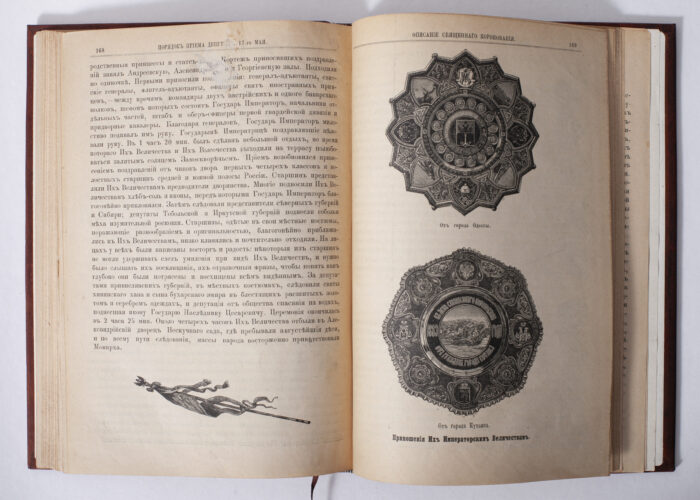 Розворот антикварної книги 1883 року з декоративними ілюстраціями та імперськими пам’ятними знаками
