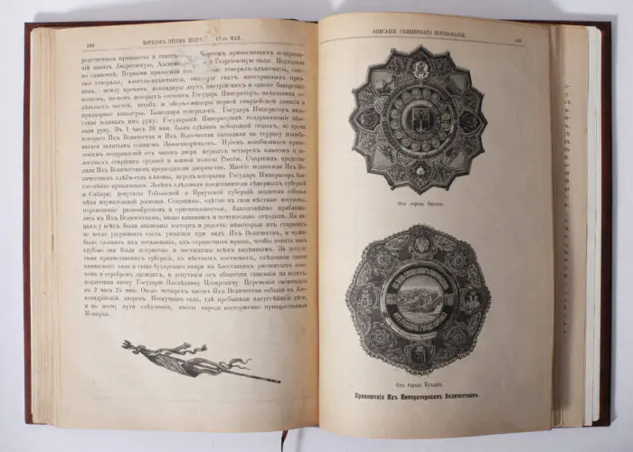 Розворот антикварної книги 1883 року з декоративними ілюстраціями та імперськими пам’ятними знаками